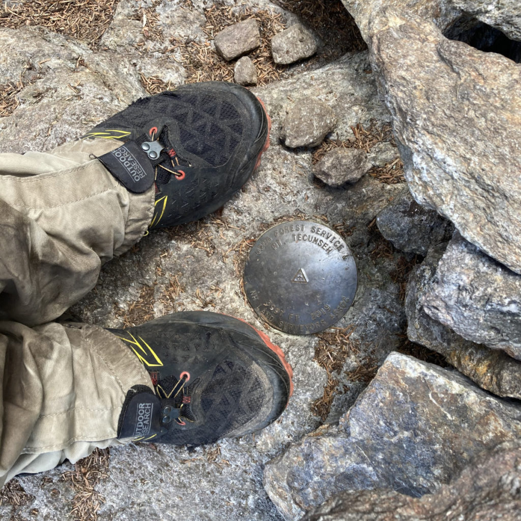 Shod feet surrounding the summit medallion on Mt Tecumseh, New Hampshire.