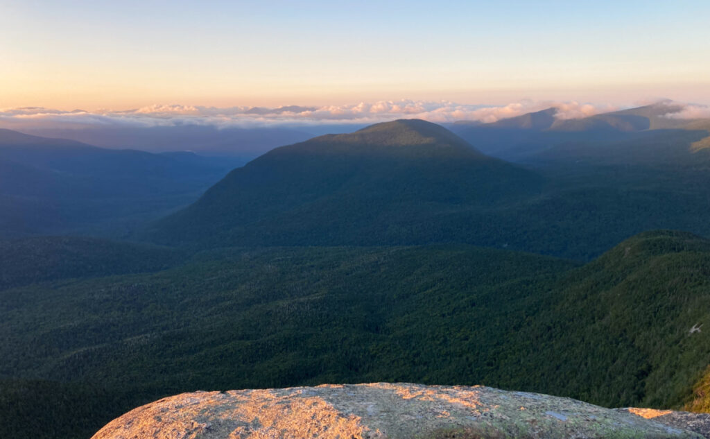 Sunrise on the summit of Owl's Head Mountain. Undercast clouds over the mountain peaks to the south. 