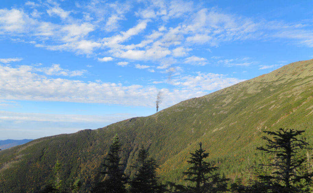 Steam locomotive of the Cog Railway belches thick black smoke as it ascends Mt Washington. 